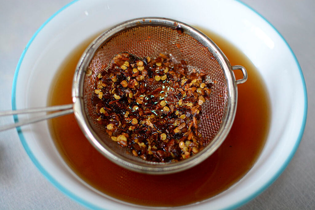 The chili flakes are filtered out of the honey with a fine sieve. 