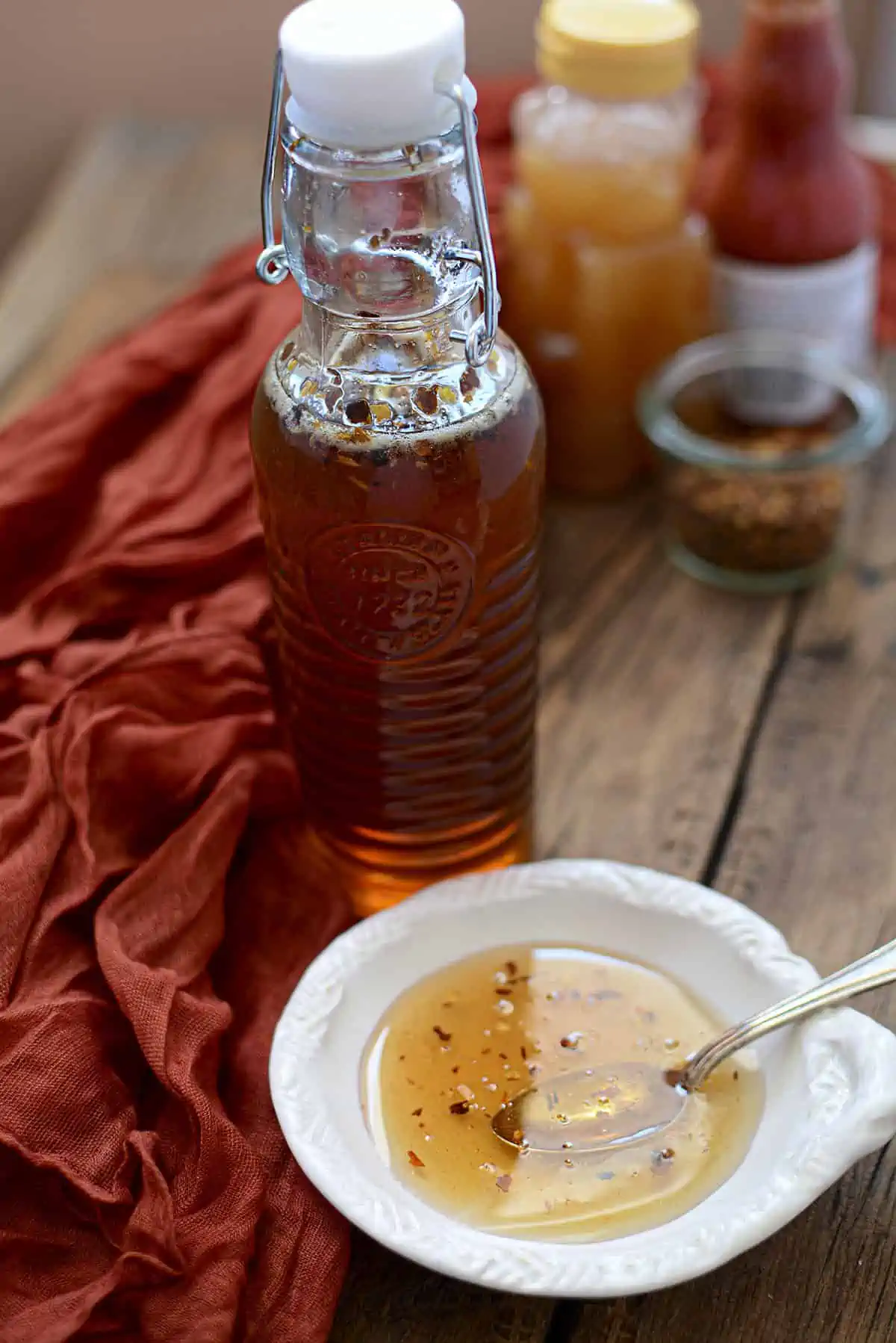 A small white bowl holds some hot honey with a larger bottle standing behind it.