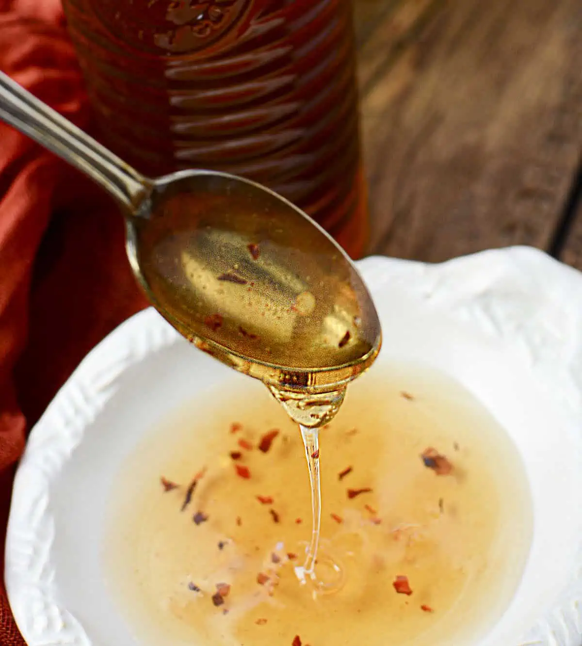 Hot honey is in a white bowl and dripping off a spoon.