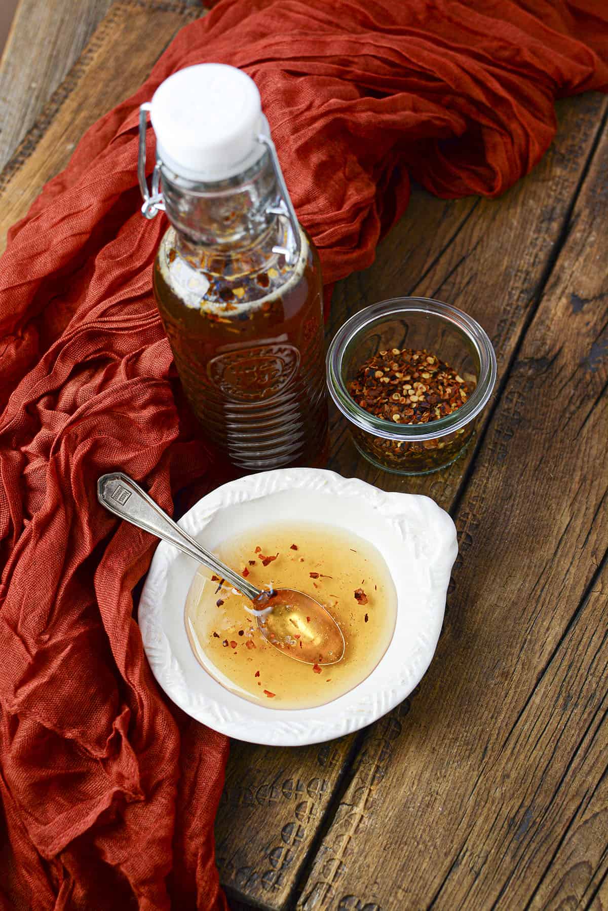 A rustic cloth lays on the left beside the bottle and small bowl of hot honey.