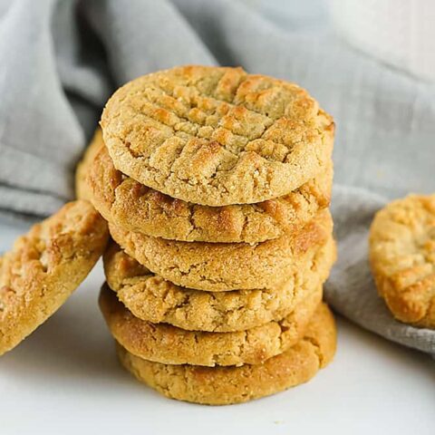 Seven peanut butter cookies stacked with two on the sides, resting on a grey napkin.