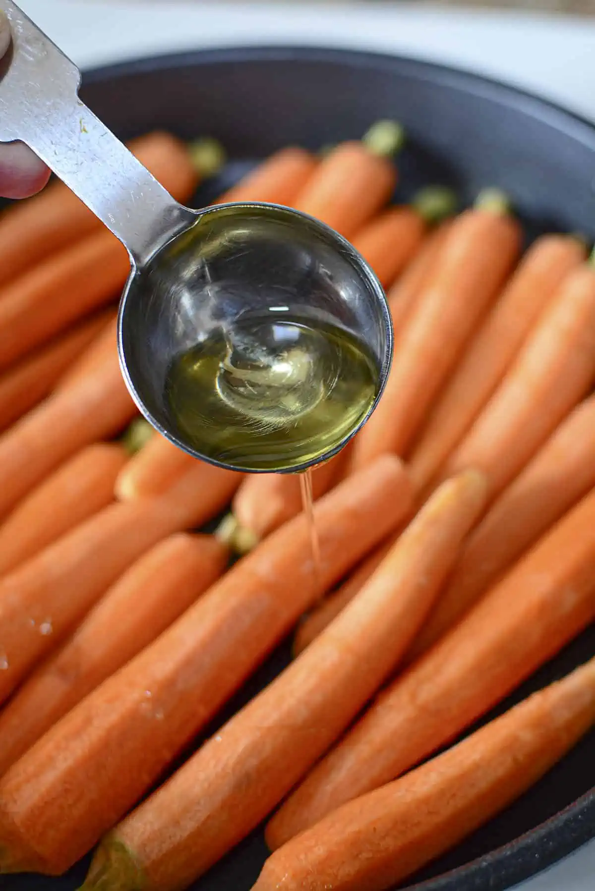 Oil being drizzled over carrots before roasting.