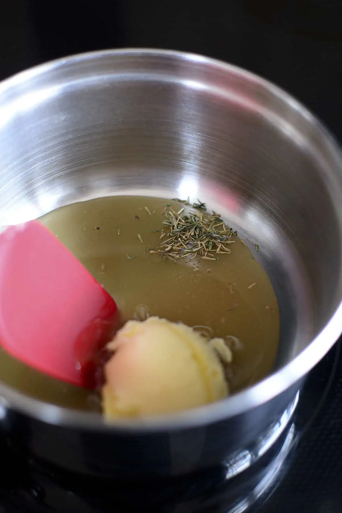 A sauce pan containing butter, hot honey, dried thyme with a red spatula ready to mix it all together to the sauce.