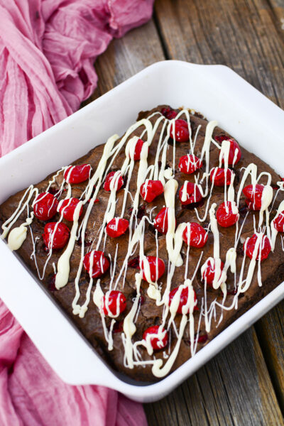 Cherry Chocolate brownies with white chocolate drizzle on top in a white baking dish.