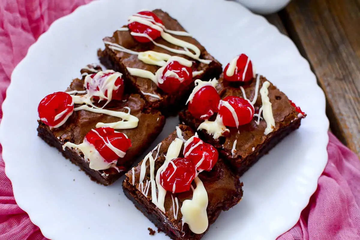 Four Cherry Chocolate Brownies on a white plate with a pink cloth.