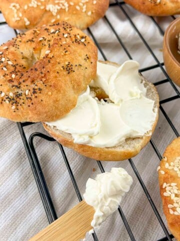 An air fryer bagel sliced open with cream cheese spread on the inside. There isa wooden knife with cream cheese on it at the bottom of the photo.
