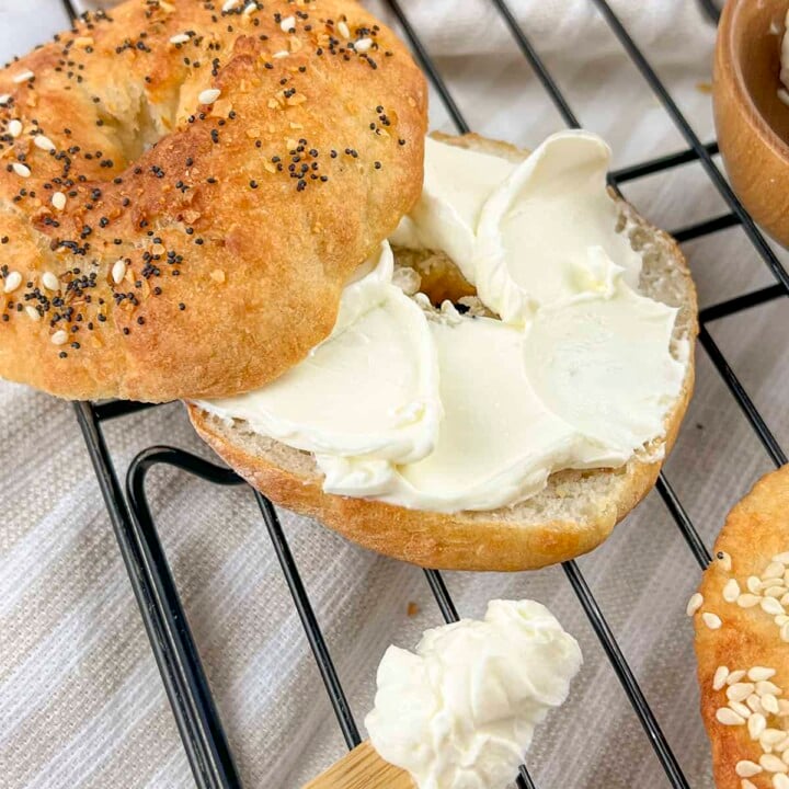 An air fryer bagel sliced open with cream cheese spread on the inside. There isa wooden knife with cream cheese on it at the bottom of the photo.
