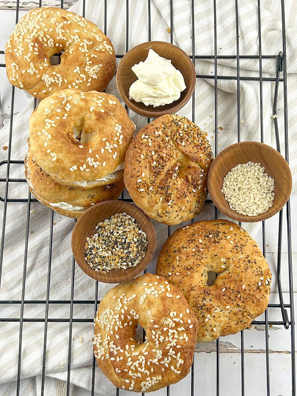 Six bagels on a cooling rack. Some with a variety of toppings and some filled with cream cheese.