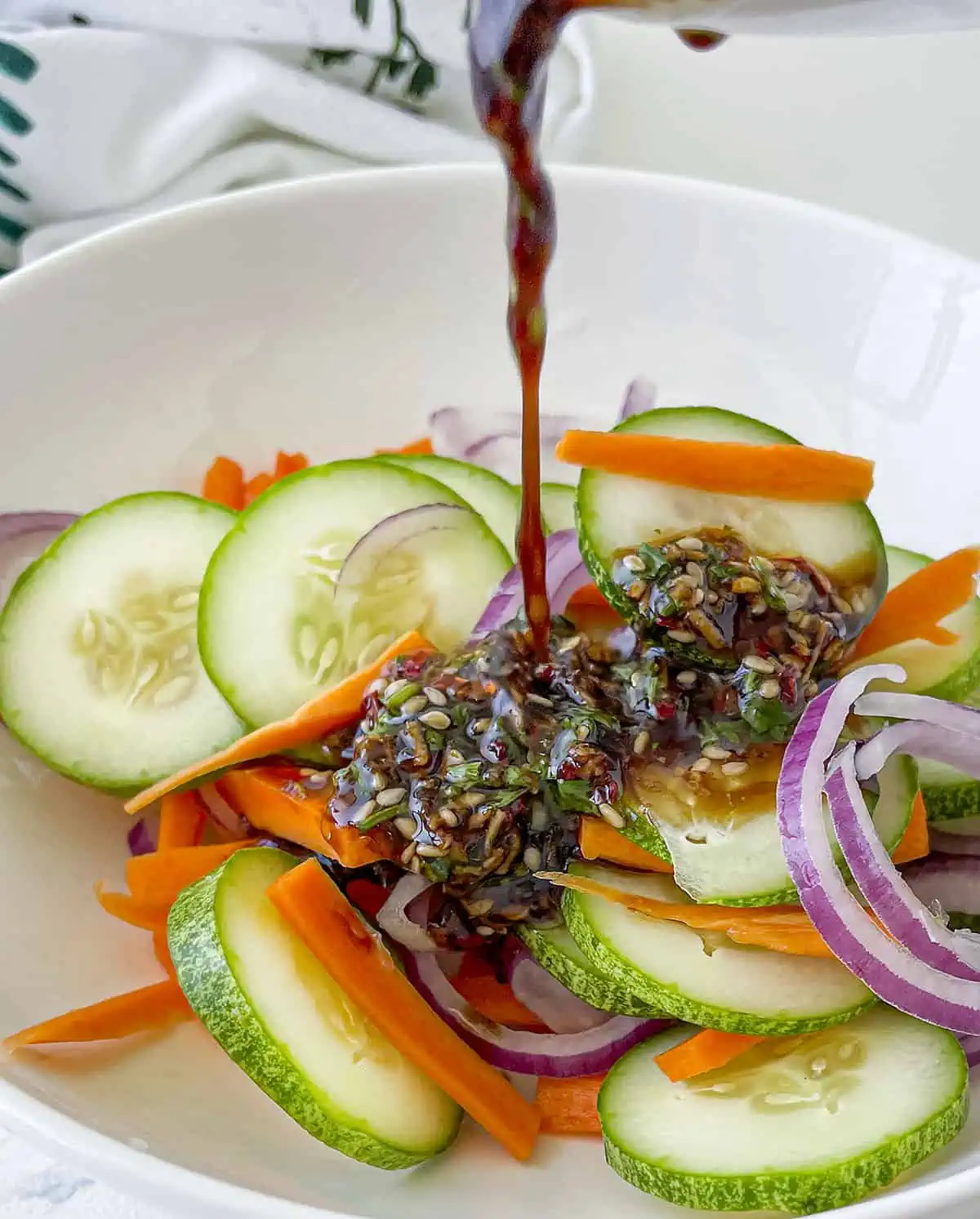 The dressing is poured over top the vegetables in a white bowl.