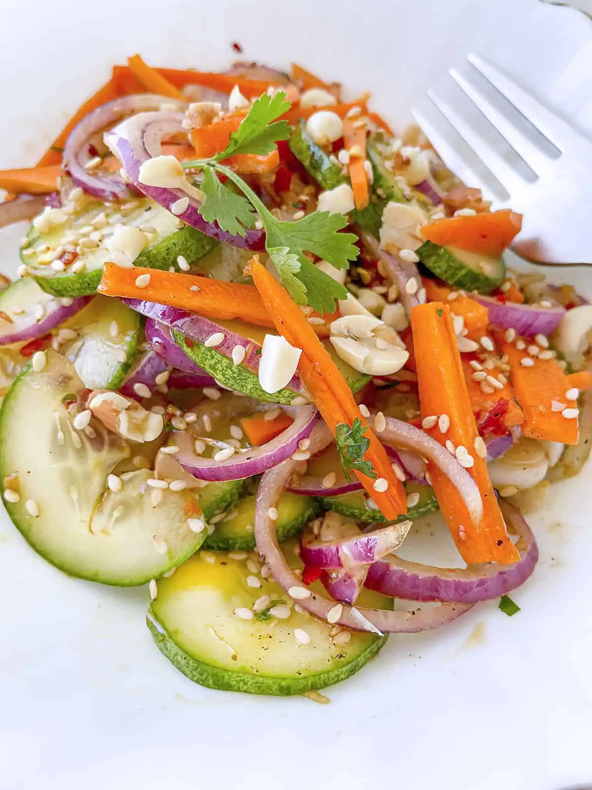 The finished carrot and cucumber salad on a white plate with a fork on the right side.