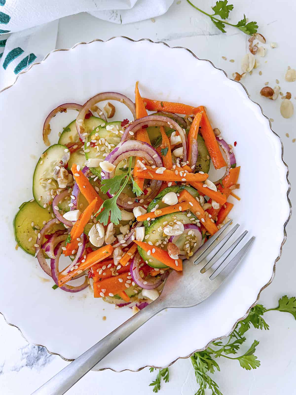 Asian carrot cucumber salad in a white bowl with a fork on the bottom right side.