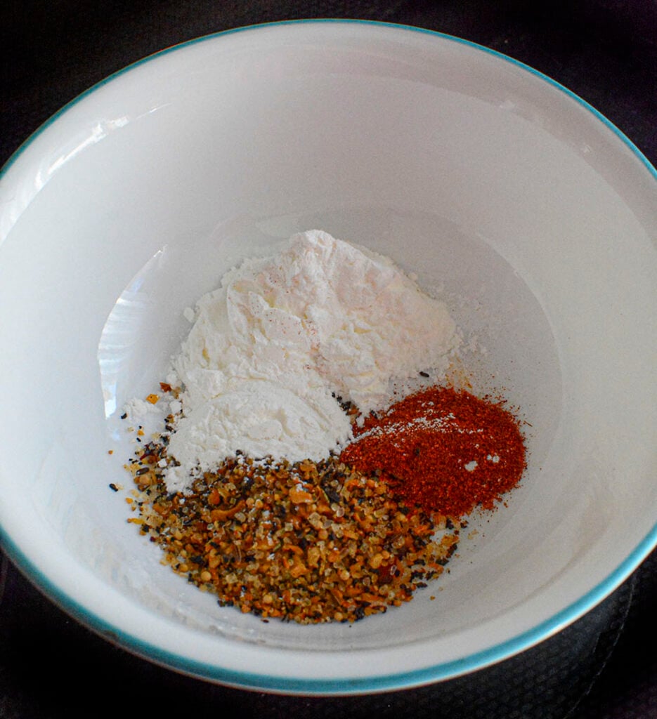 All the seasonings and flour needed to season and dredge the chicken in a white bowl with a blue rim.