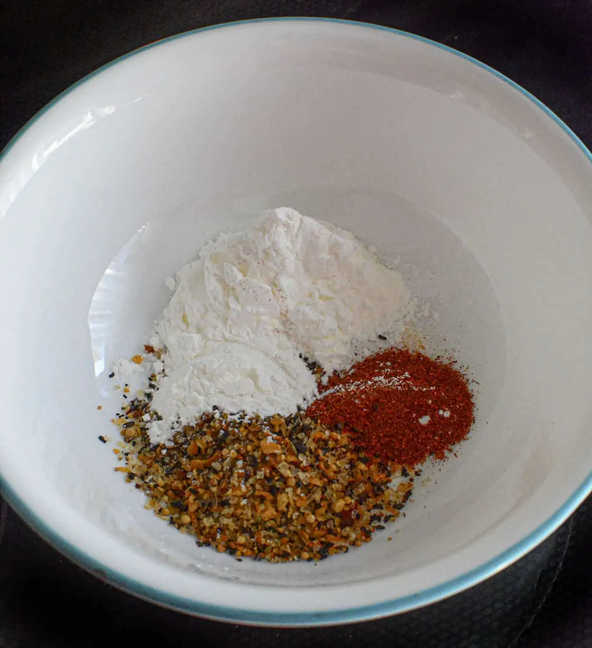 Seasoning spices in a white bowl. Cornstarch, smoked paprika, montreal chicken seasoning.