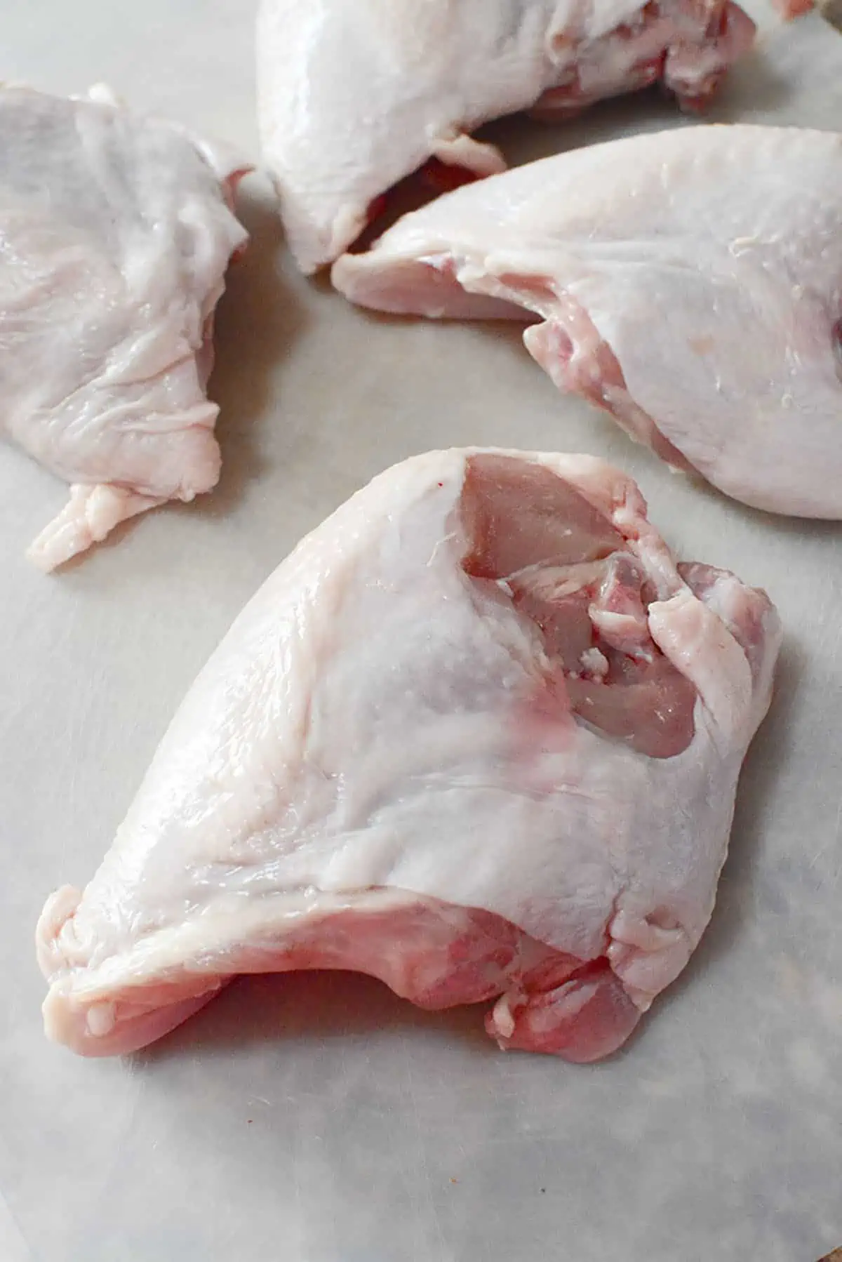 3 raw bone in chicken breasts with the skin still attached on a white plastic cutting board.