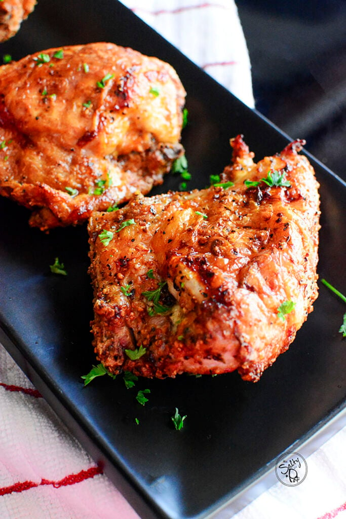 One main cooked chicken breast with another behind it on a plate with a white and red napkin underneath.