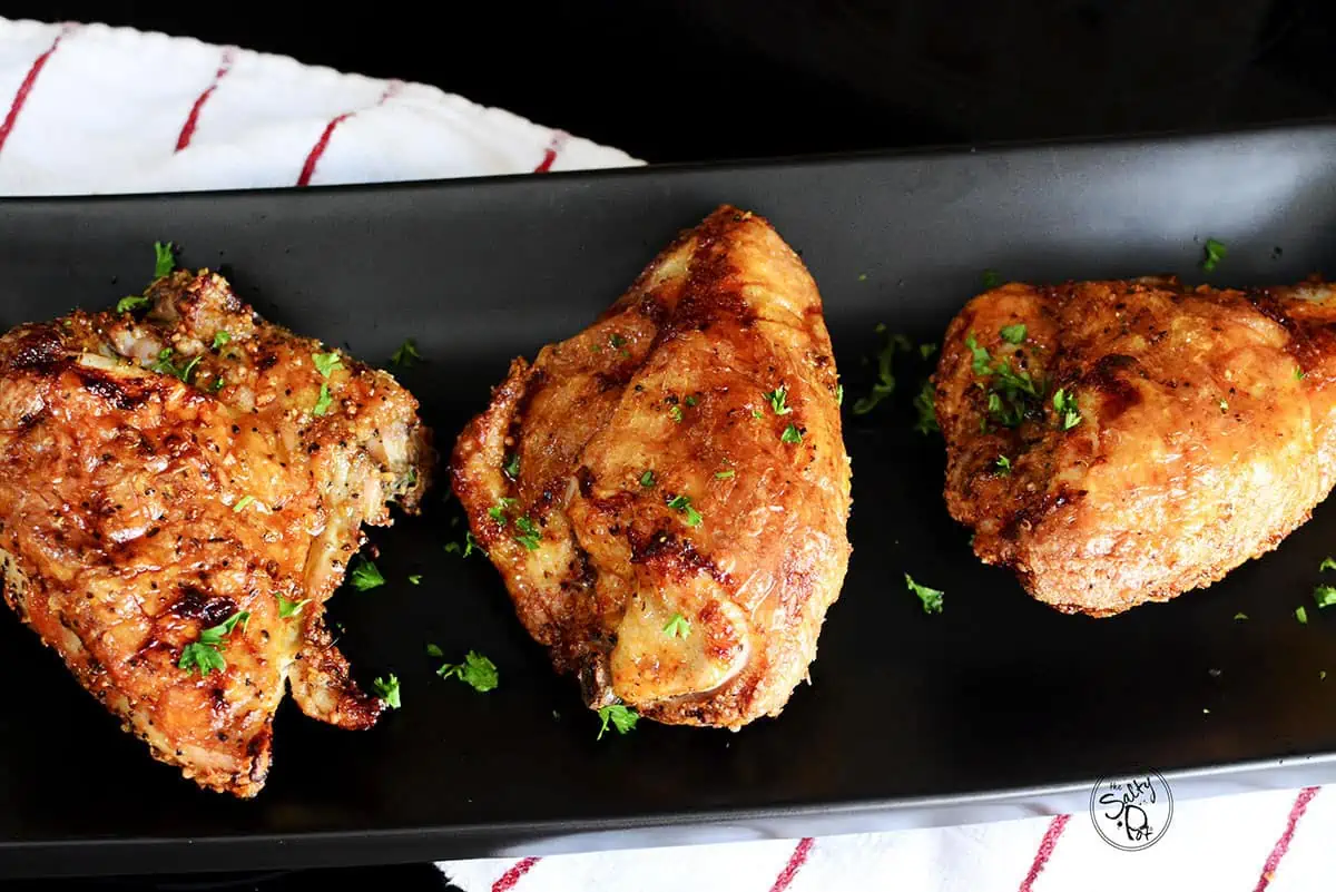 Three air fried chicken breasts on a plate with green parsley sprinkled on top.