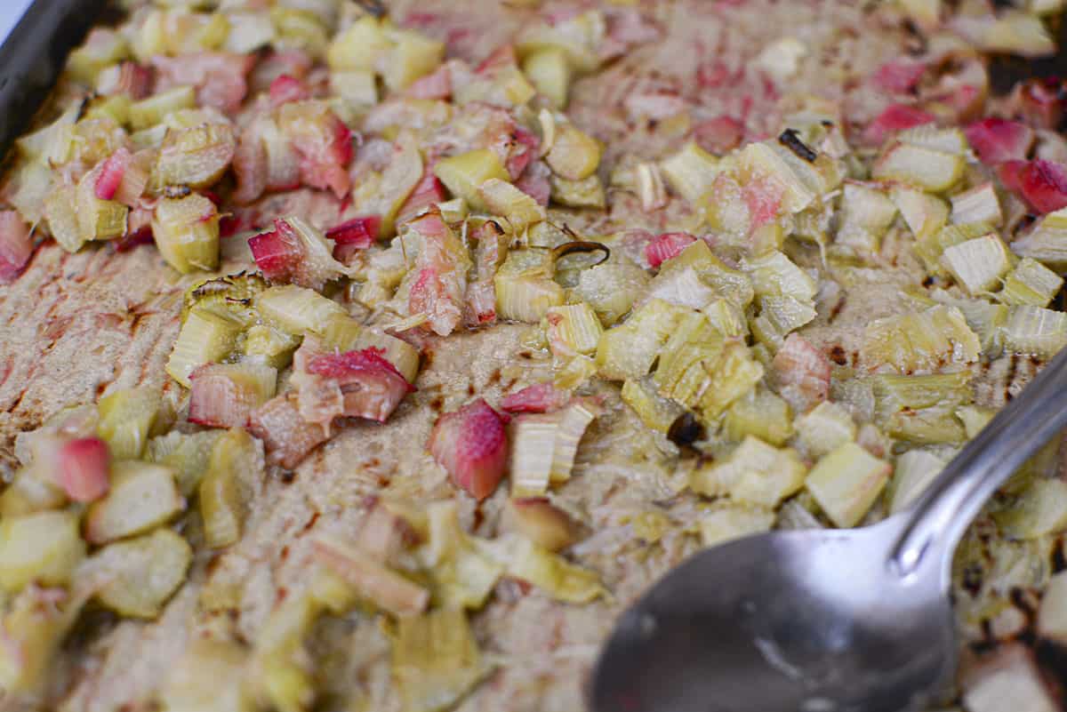 Chopped rhubarb and onions soft from the oven after being roasted with a spoon in the bottom right corner.