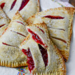 Strawberry rhubarb handpies on a decorative plate. One hand pie is broke open to see the filling inside.