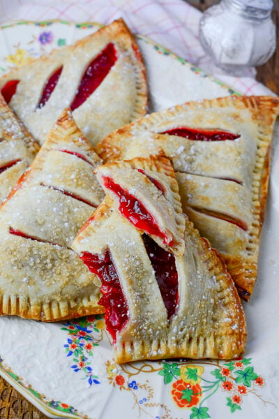 Strawberry rhubarb handpies on a decorative plate. One hand pie is broke open to see the filling inside.