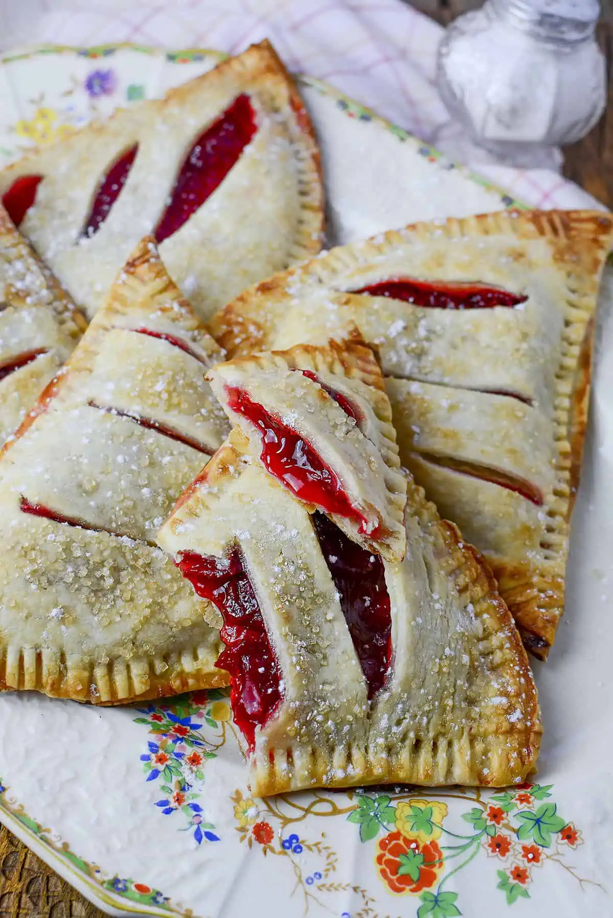 Strawberry rhubarb handpies on a decorative plate. One hand pie is broke open to see the filling inside.