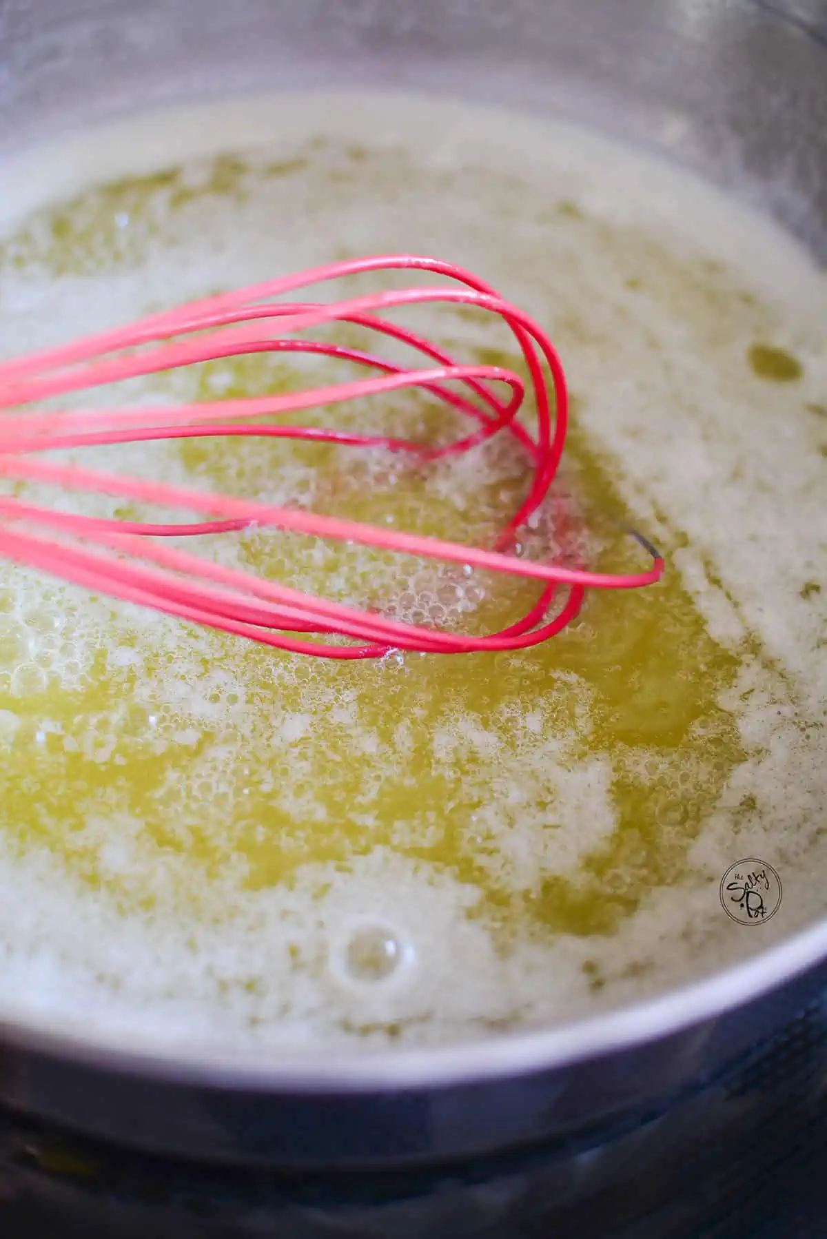 The butter is completely melted and a red whisk is moving the butter around so it doesn't burn in the pan.