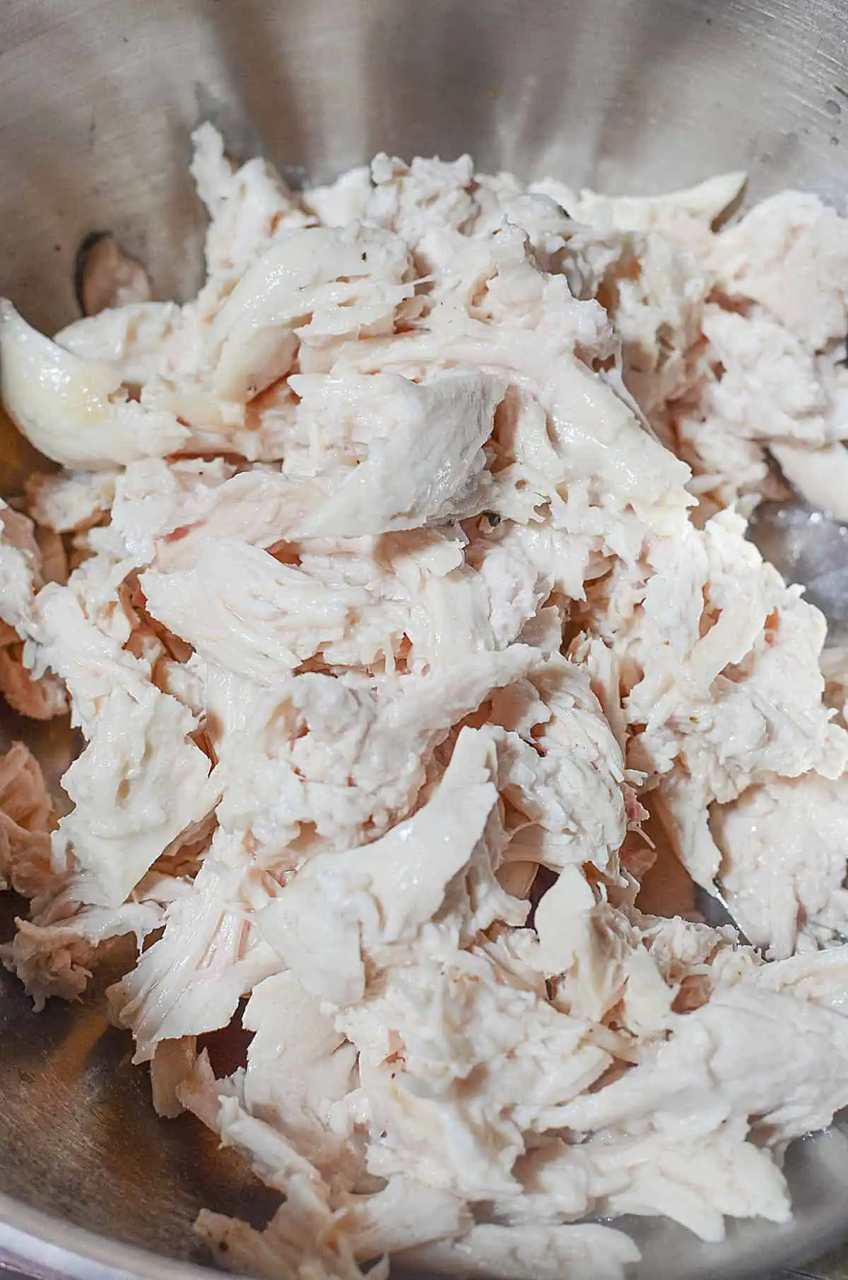 Cooked chicken in a silver bowl, ready to go into the casserole recipe.