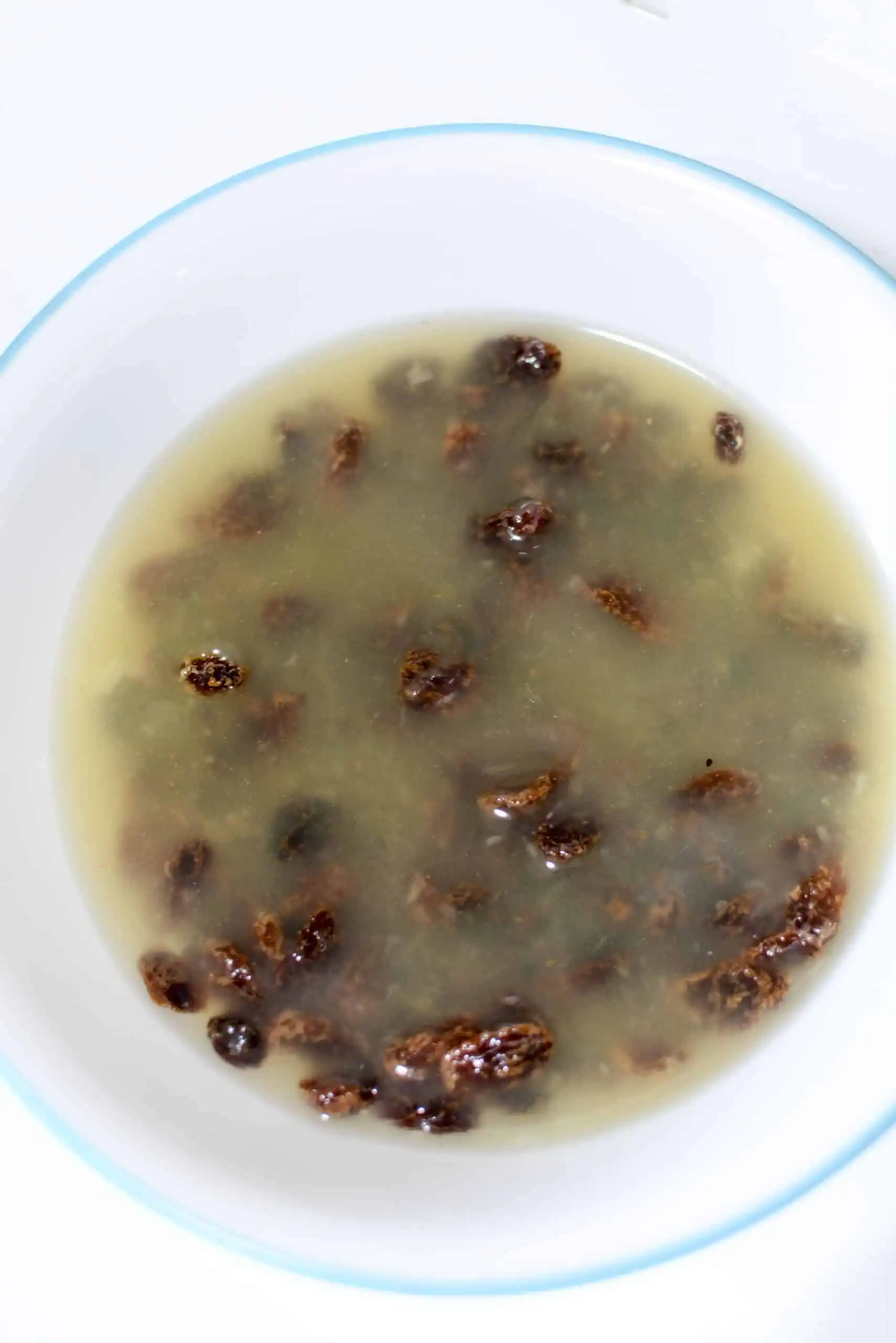 Raisins soaking in the reserved pineapple juice in a white bowl. 