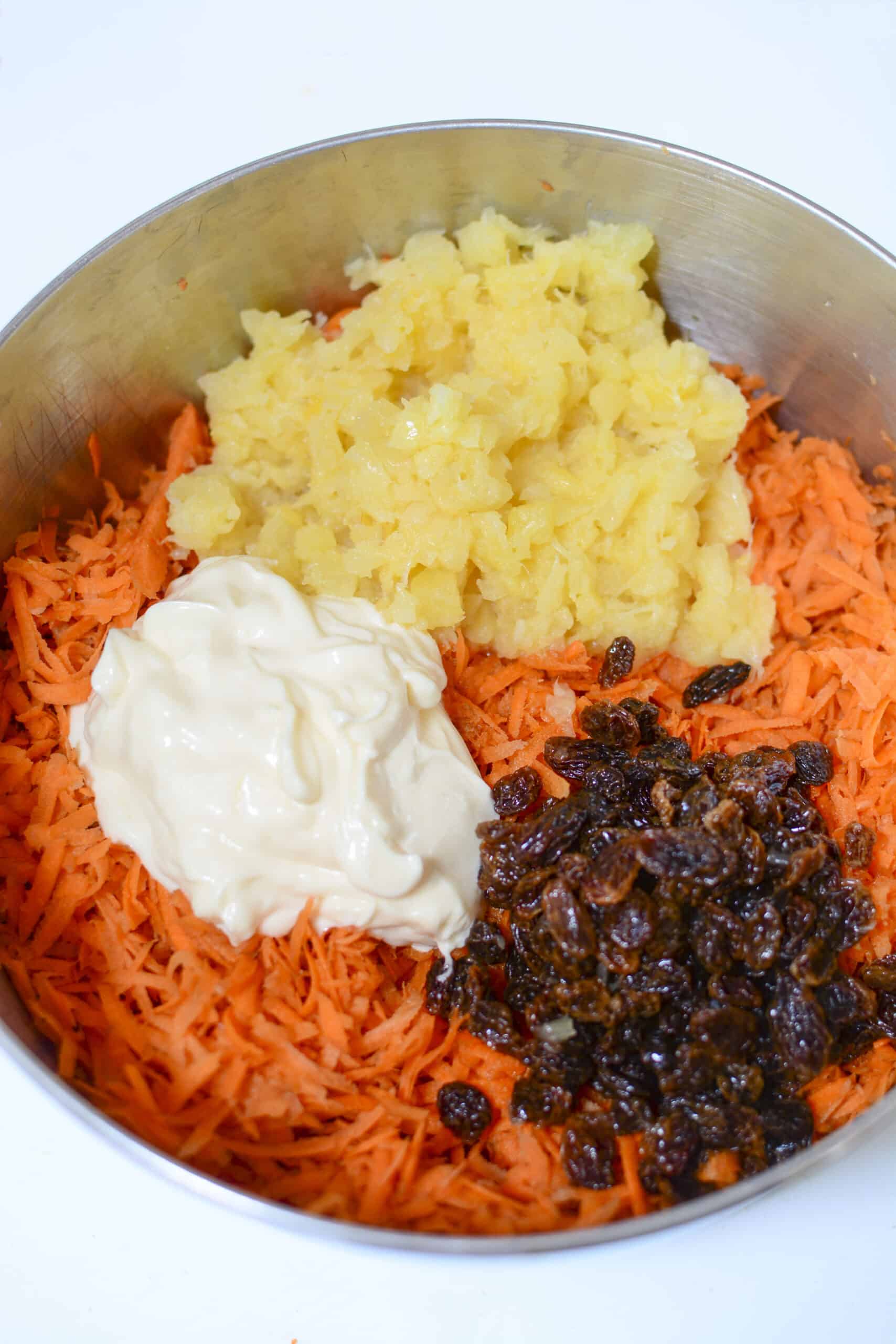 Carrot and pineapple salad dressing ingredients in the bowl on top of the carrots.