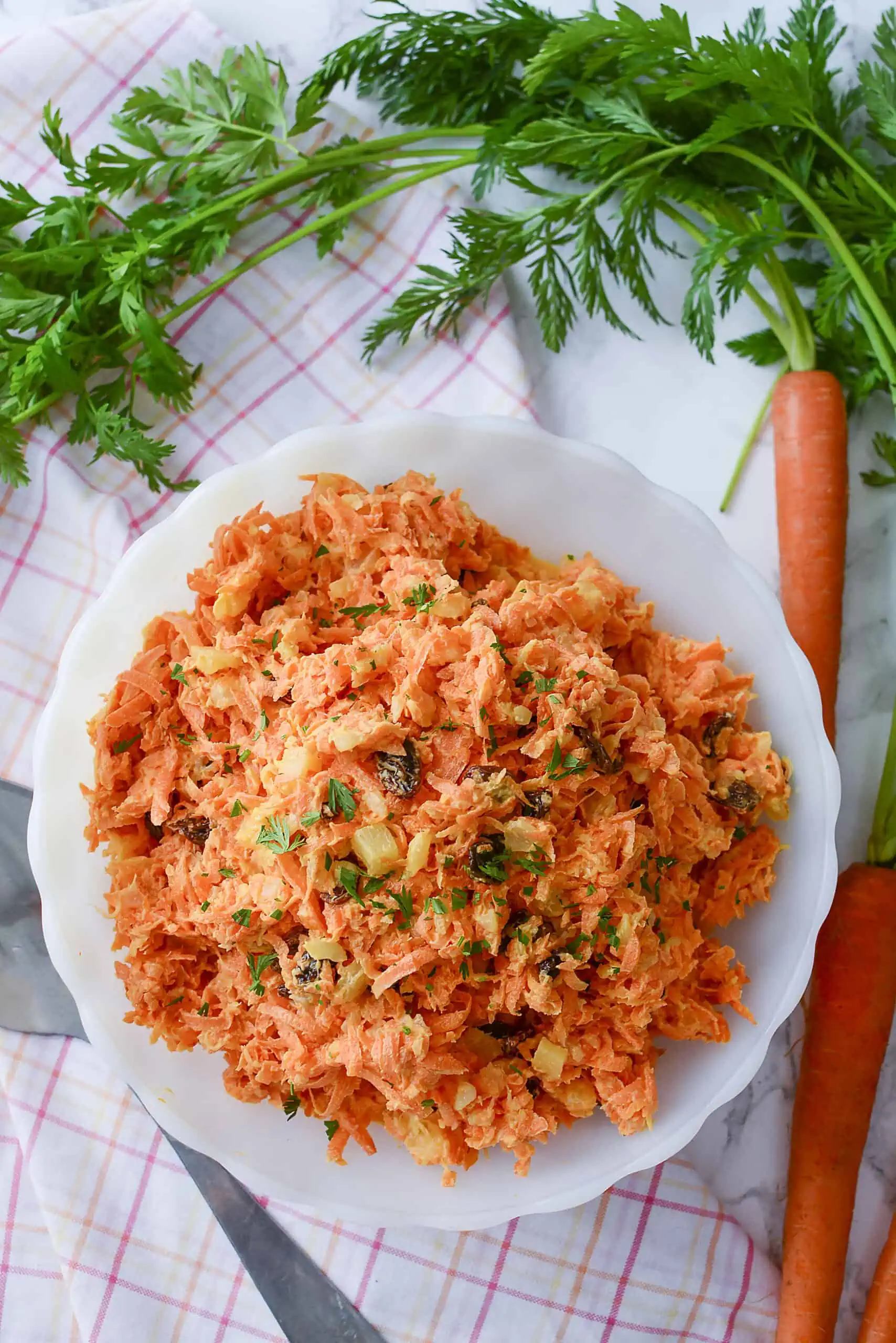 An overhead photo of the carrot salad with whole carrots draped above the bowl on the table. 