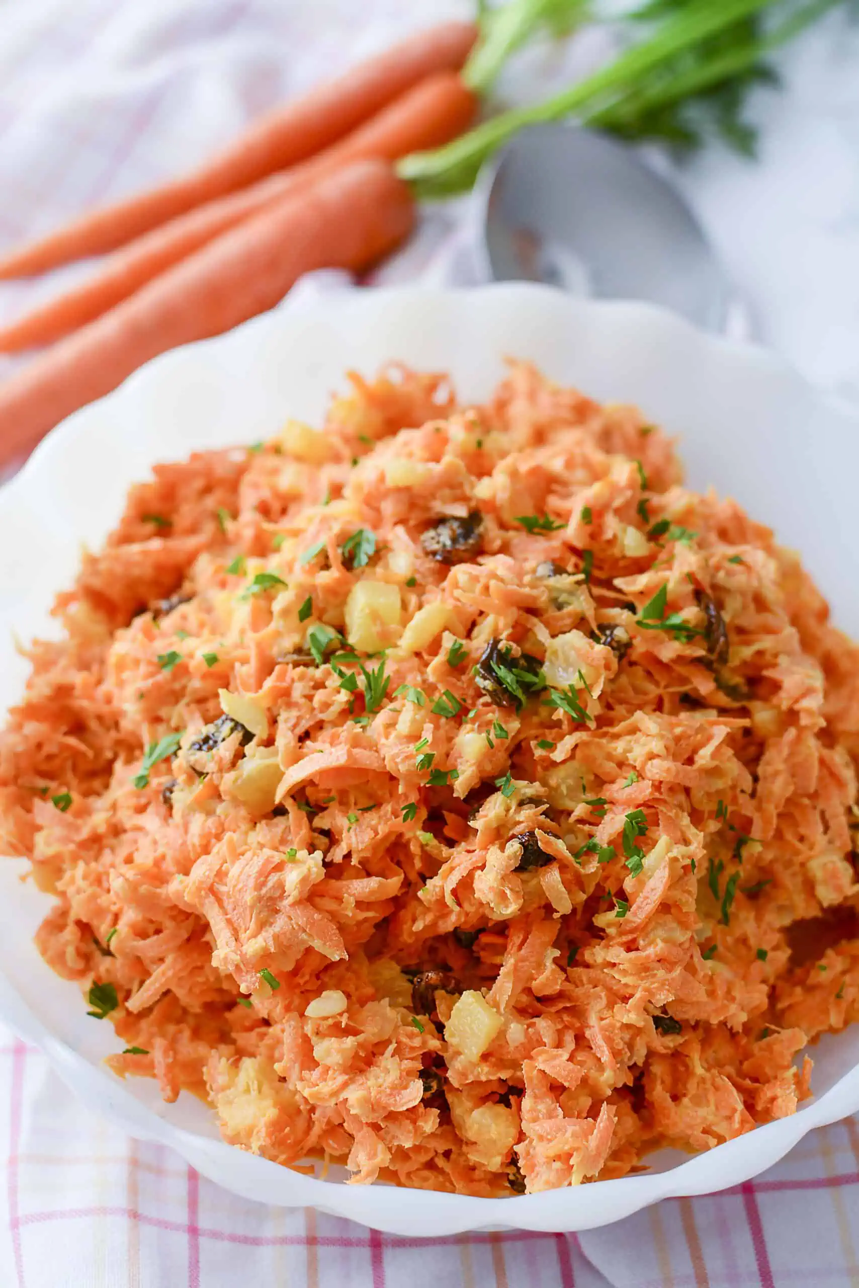 Carrot salad with raisins and pineapple in a white bowl with parsley sprinkled on top.