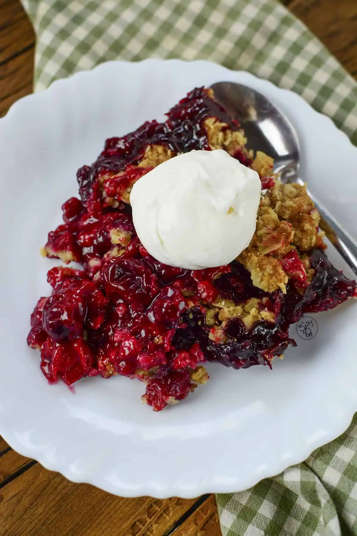 Sour cherry crisp on a white plate with whipped cream on top.