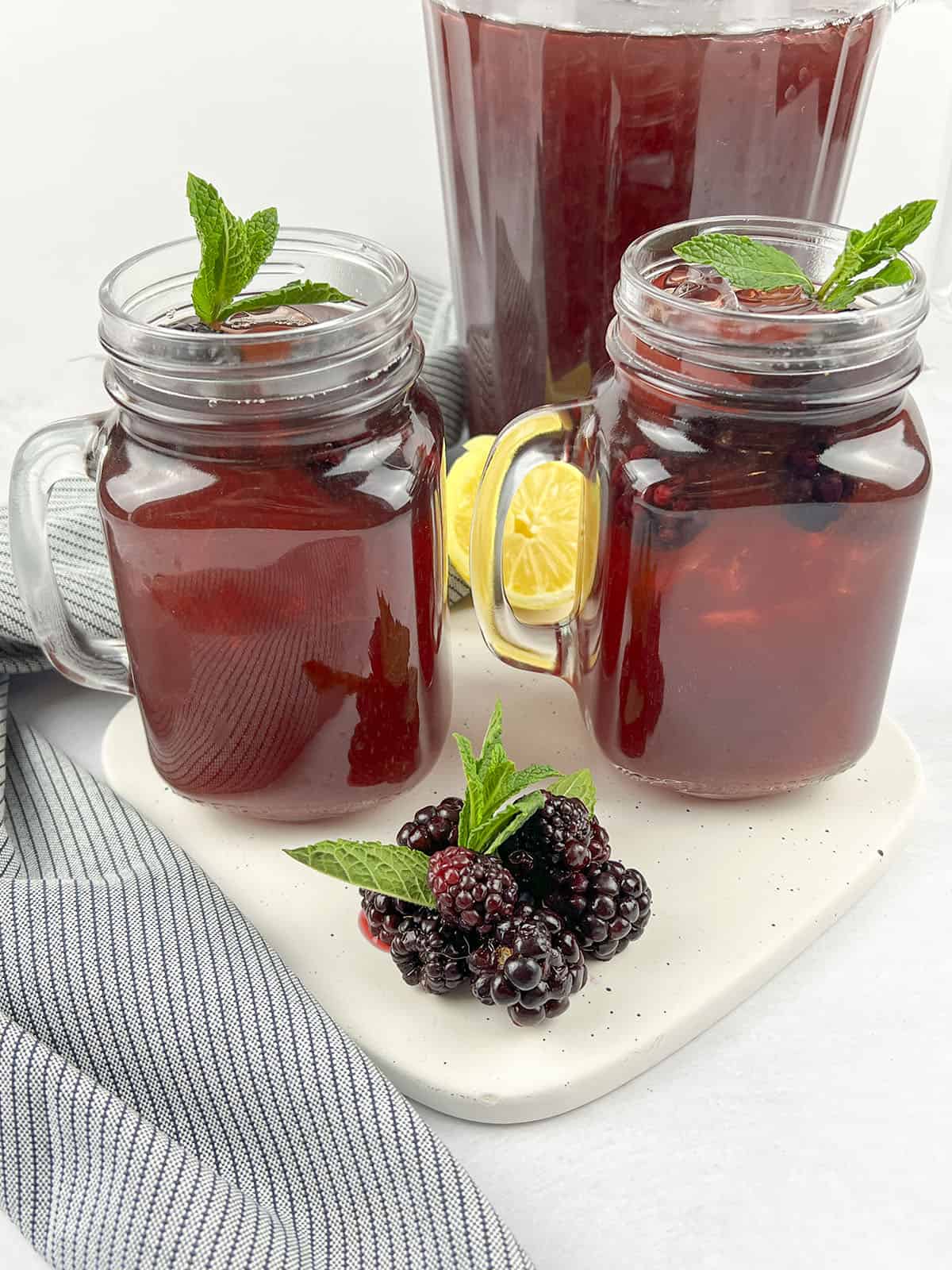 Two glasses and a pitcher of blackberry tea on a white cutting board.