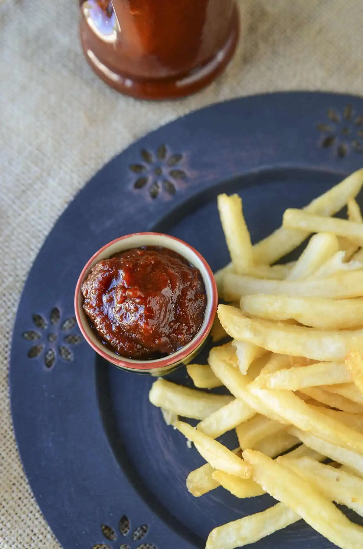 Ketchup in a small ramekin next to some french fries on a black plate.