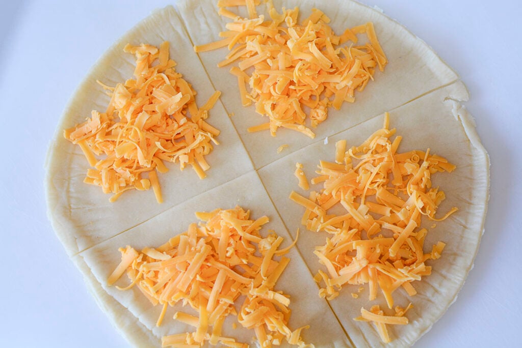 Shredded cheddar is added to each pie section.