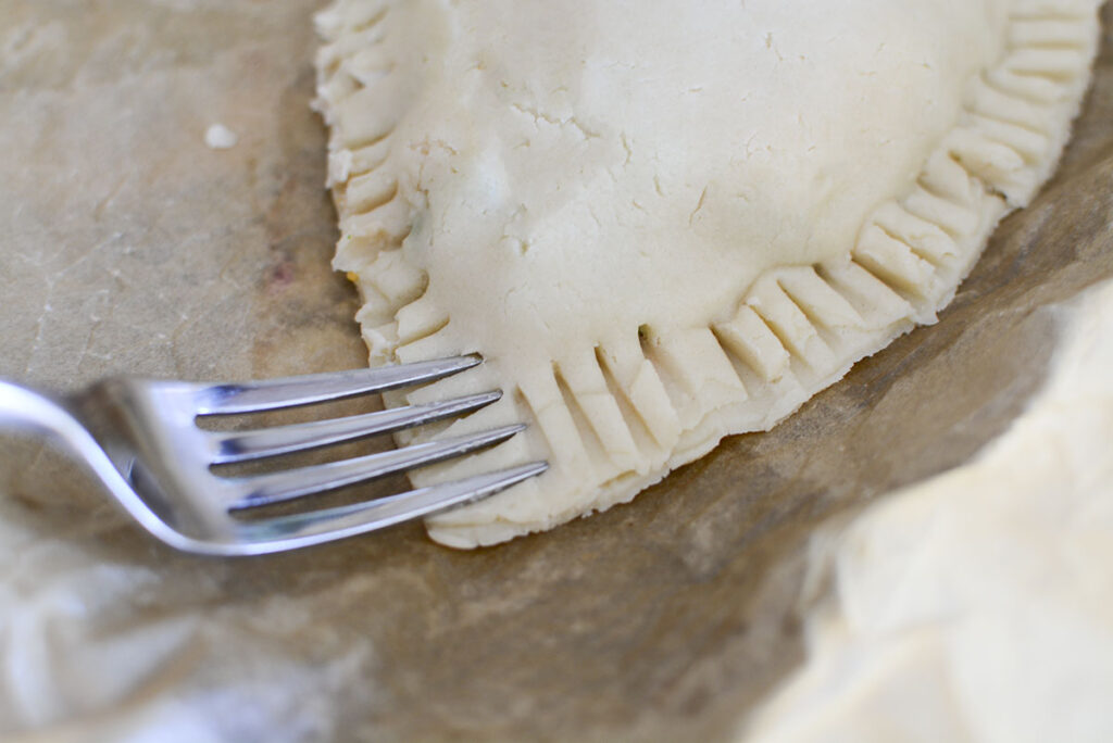 A fork is sealing the pie crust edges with the filling inside.