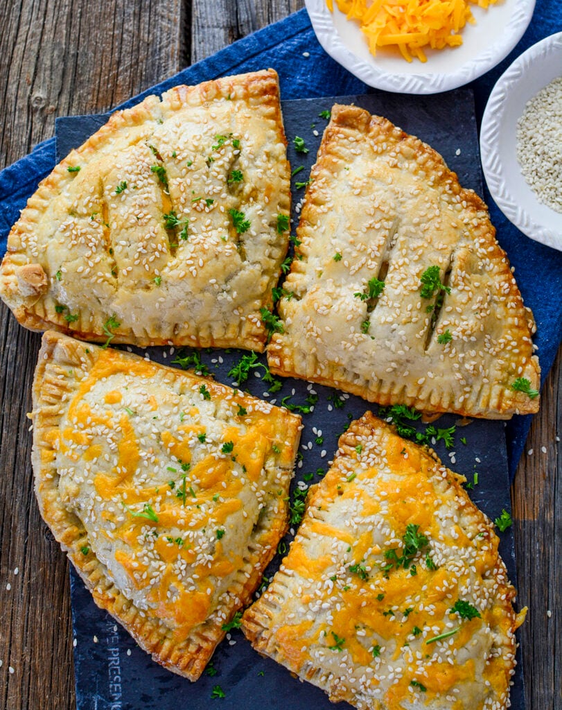 Four hand pies with cheddar and sesame seed toppings on a blue napkin.