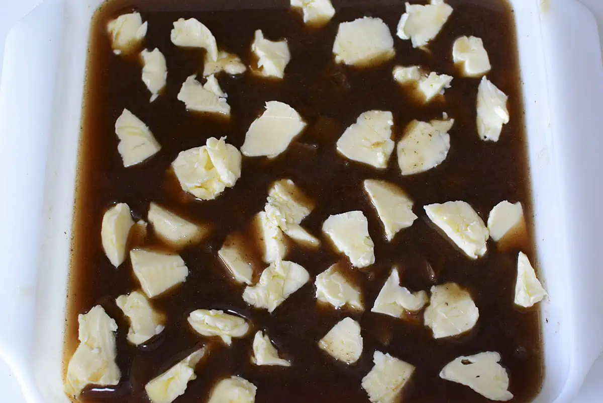 The stick of butter has been broken up into small pieces and topped on top of the rice mixture.