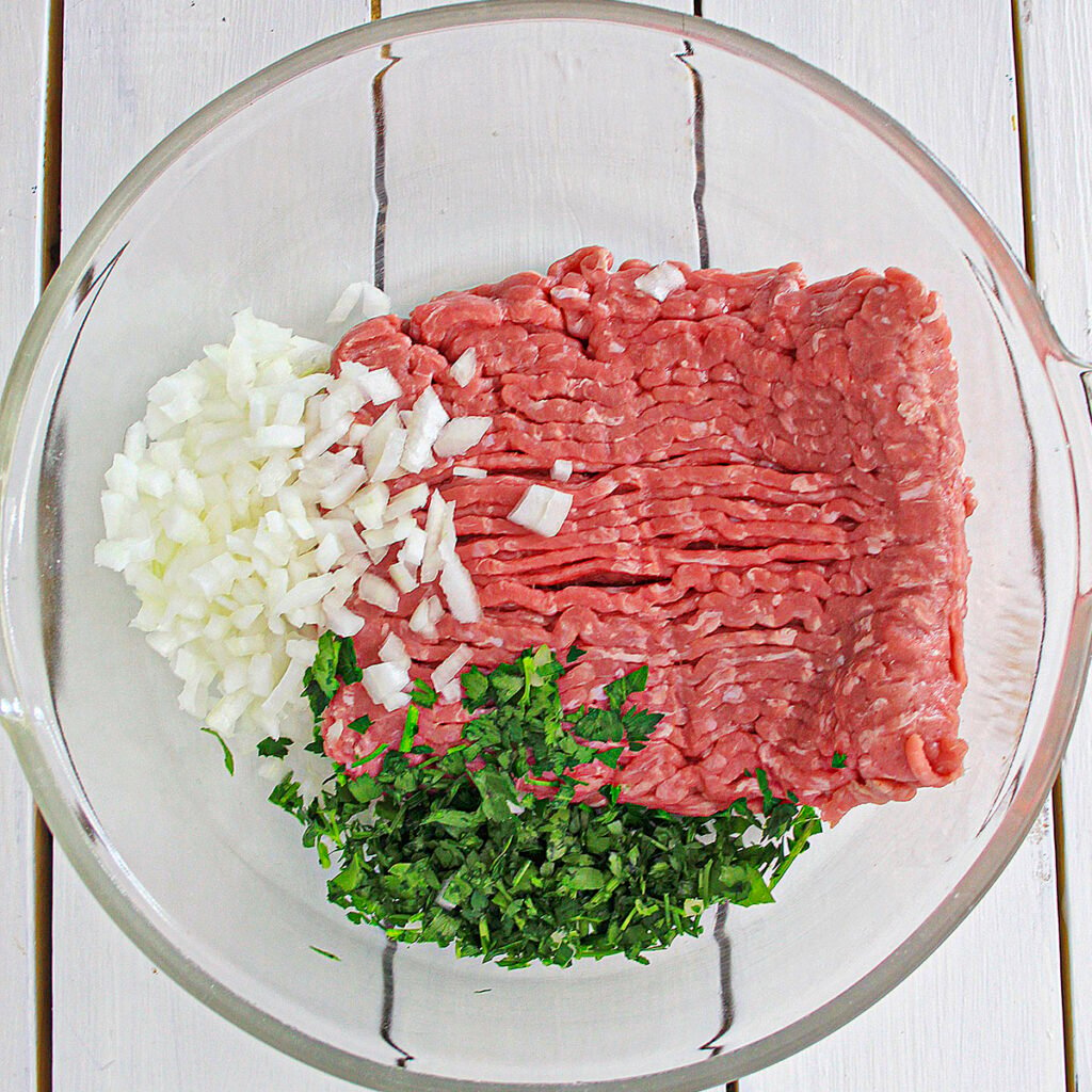 Ground chicken, onions and parsley in a clear bowl.