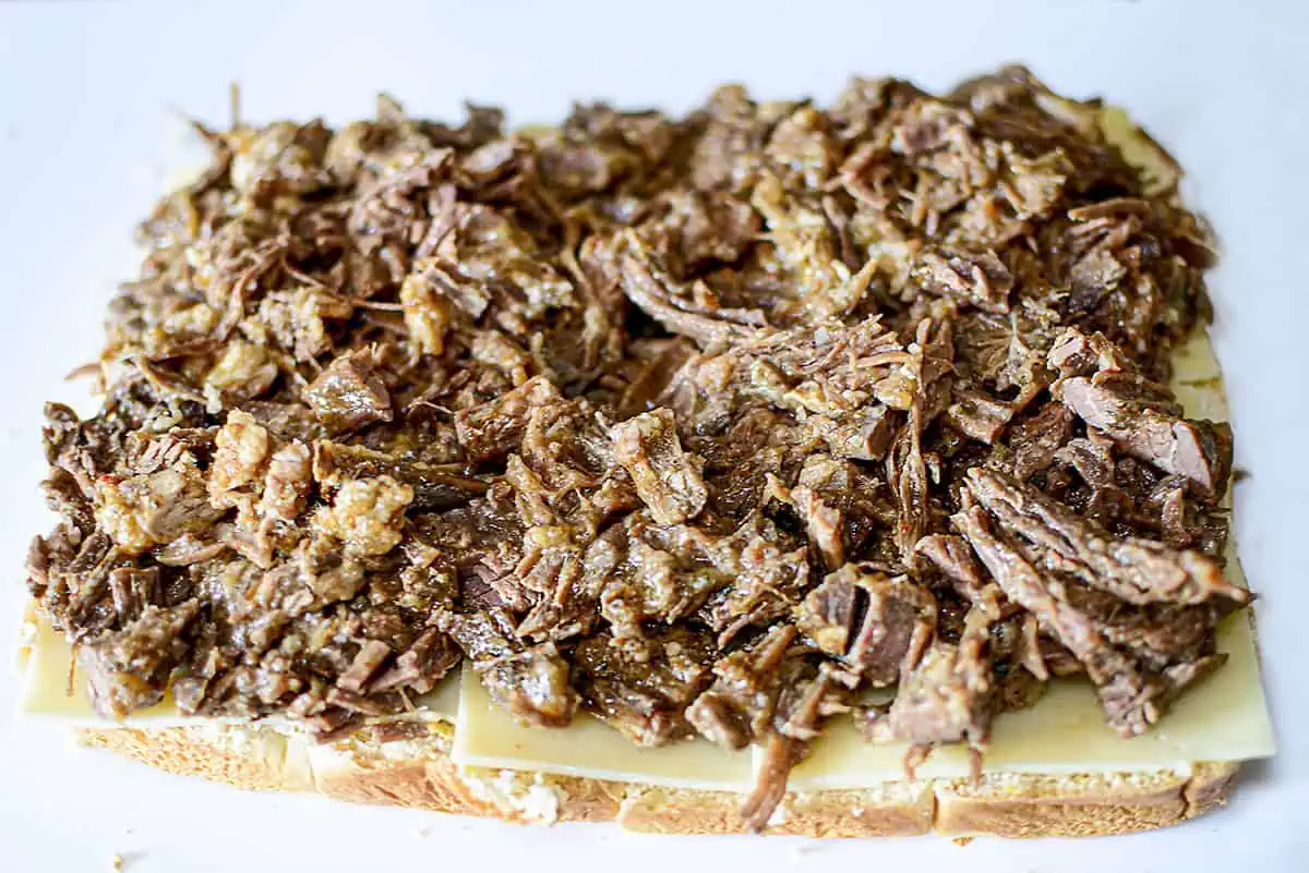 Topping the cheese with shredded brisket.