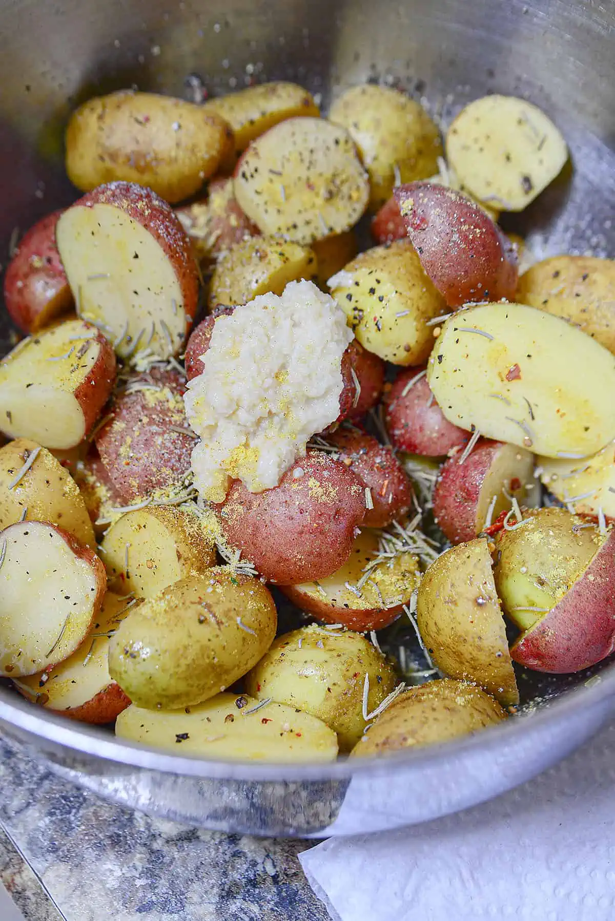 Mixing together the potatoes, pepper, rosemary and garlic in a silver bowl.