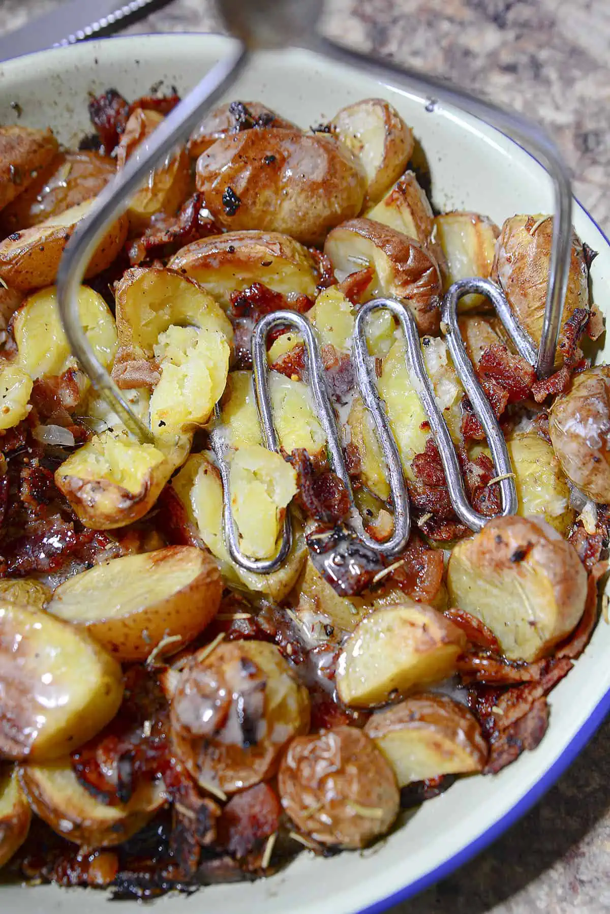 Mashing the roasted potatoes with a potato masher. 