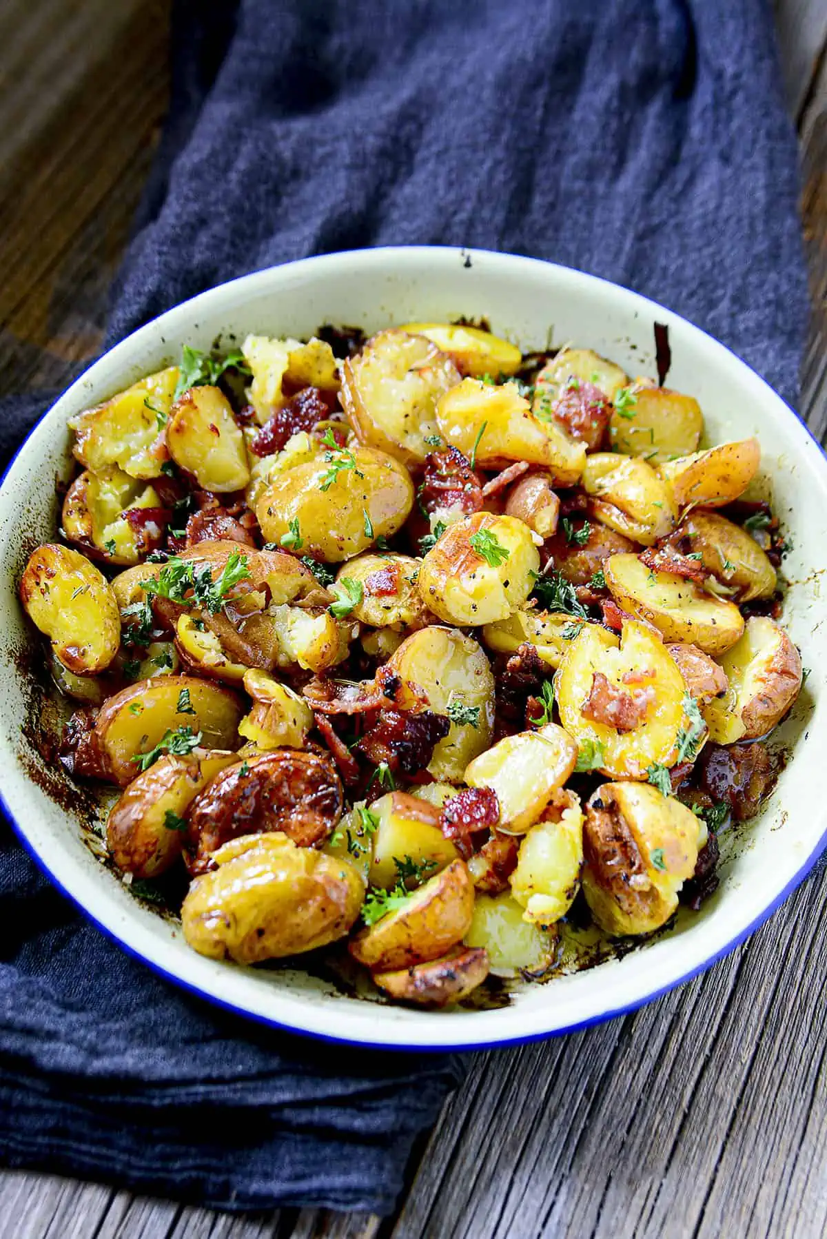 Roasted potatoes with bacon in a blue pie plate with a blue napkin underneath.