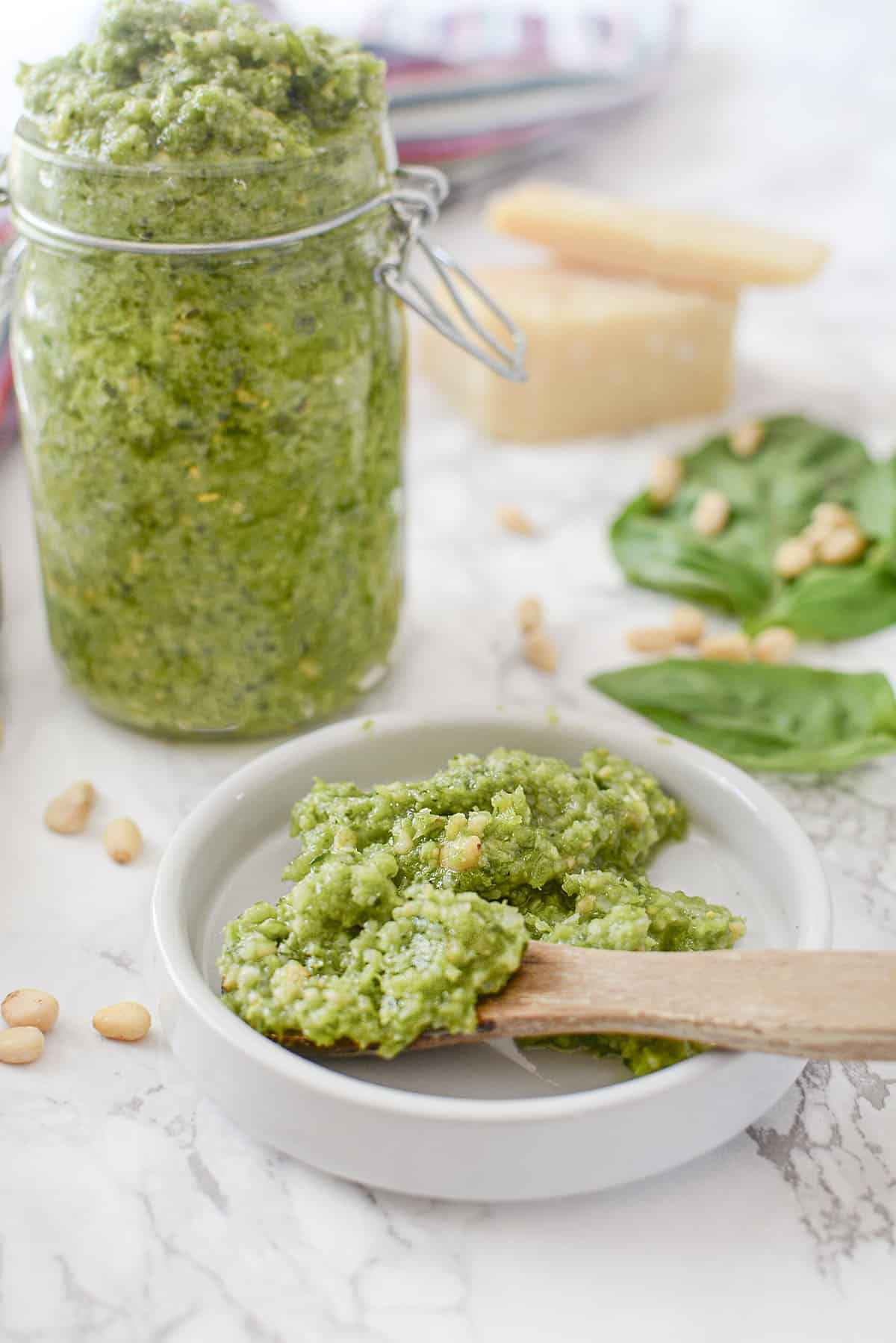 Garlic scape pesto in a small white bowl with a wooden spoon sticking out to the right.