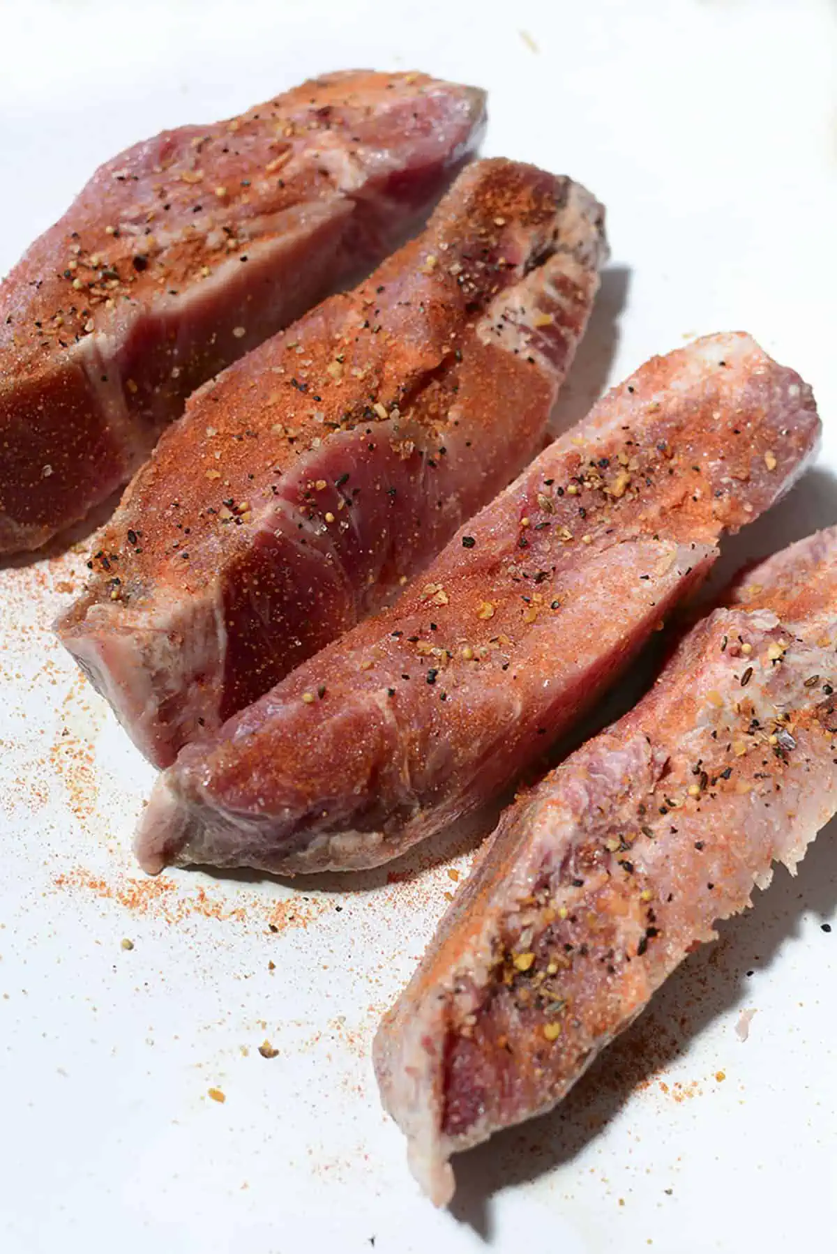 Four ribs seasoned and resting on a white plastic cutting board.