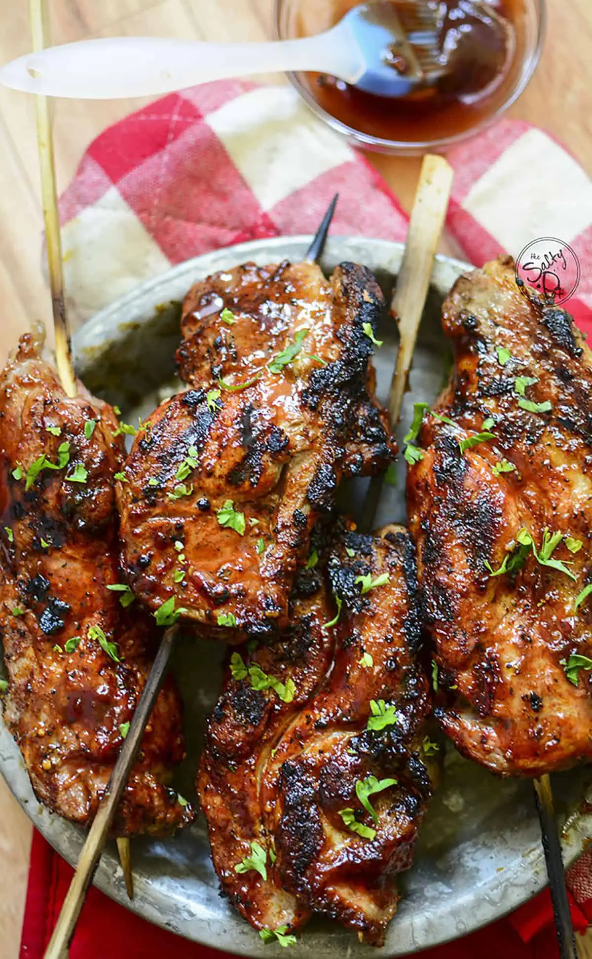 Ribs in a tin plate with a small bowl of extra bbq sauce at the top.