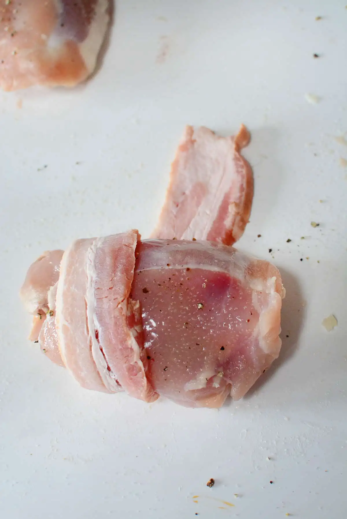 Wrapping a slice of bacon around a seasoned chicken thigh.