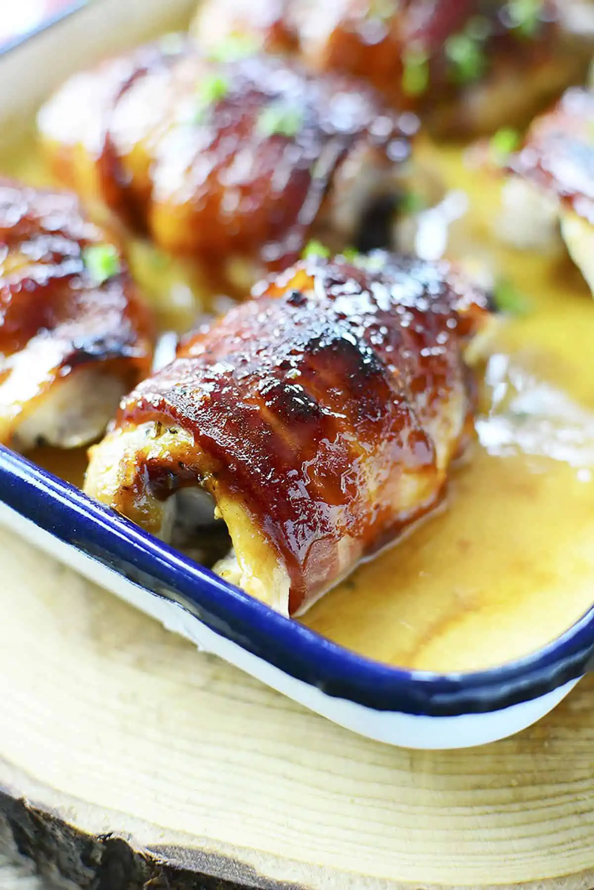 One cooked bbq chicken thigh that is surrounded by a few others, sits in a baking dish.