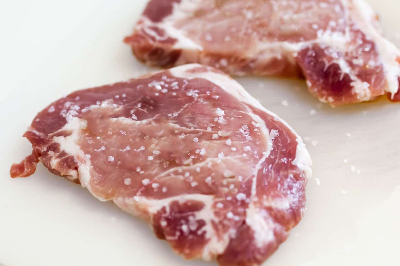 Raw pork steaks sprinkled with salt.