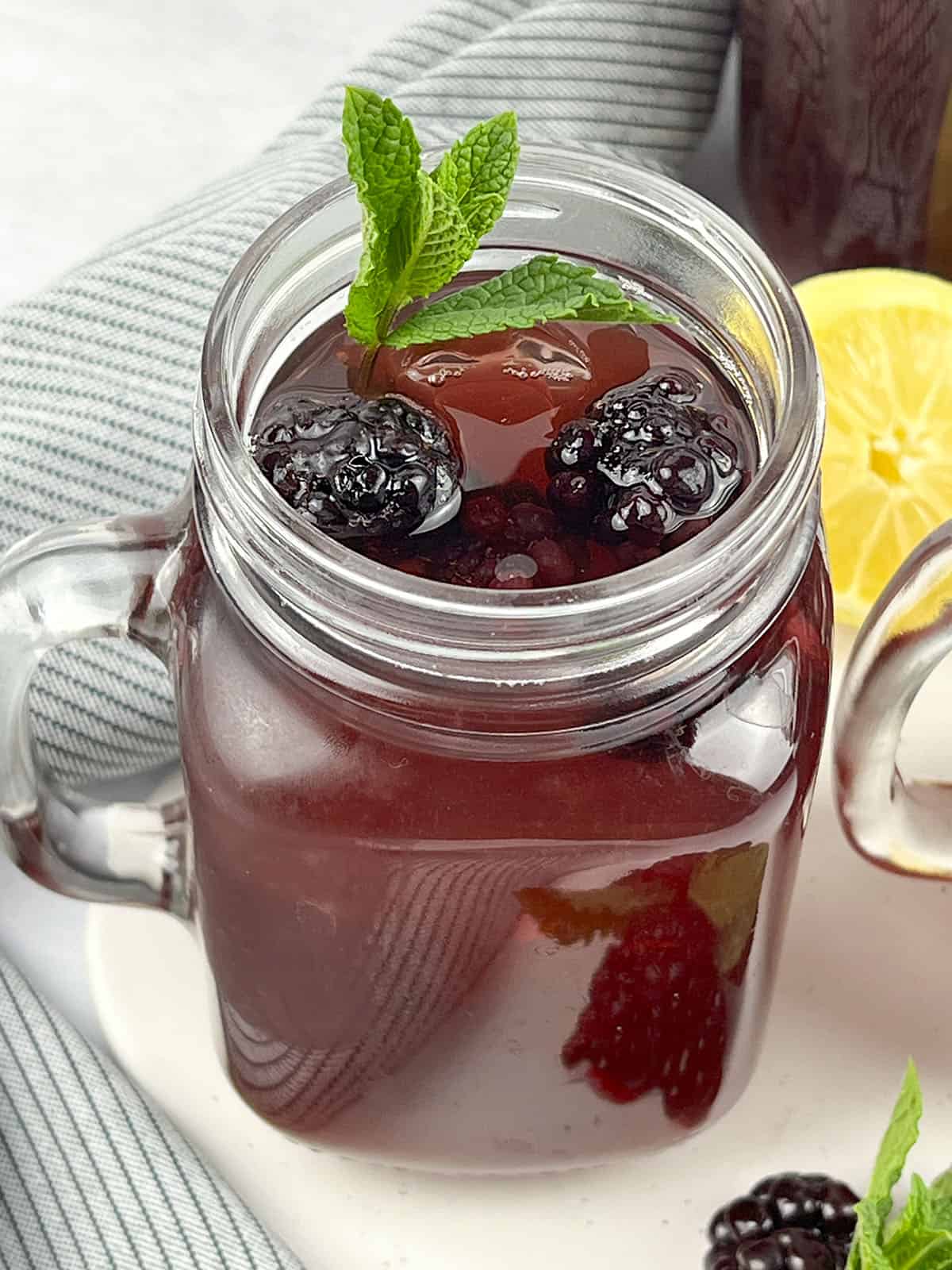 One glass of sweet tea with blackberries on a white tray. There is a lemon in the background on the right.