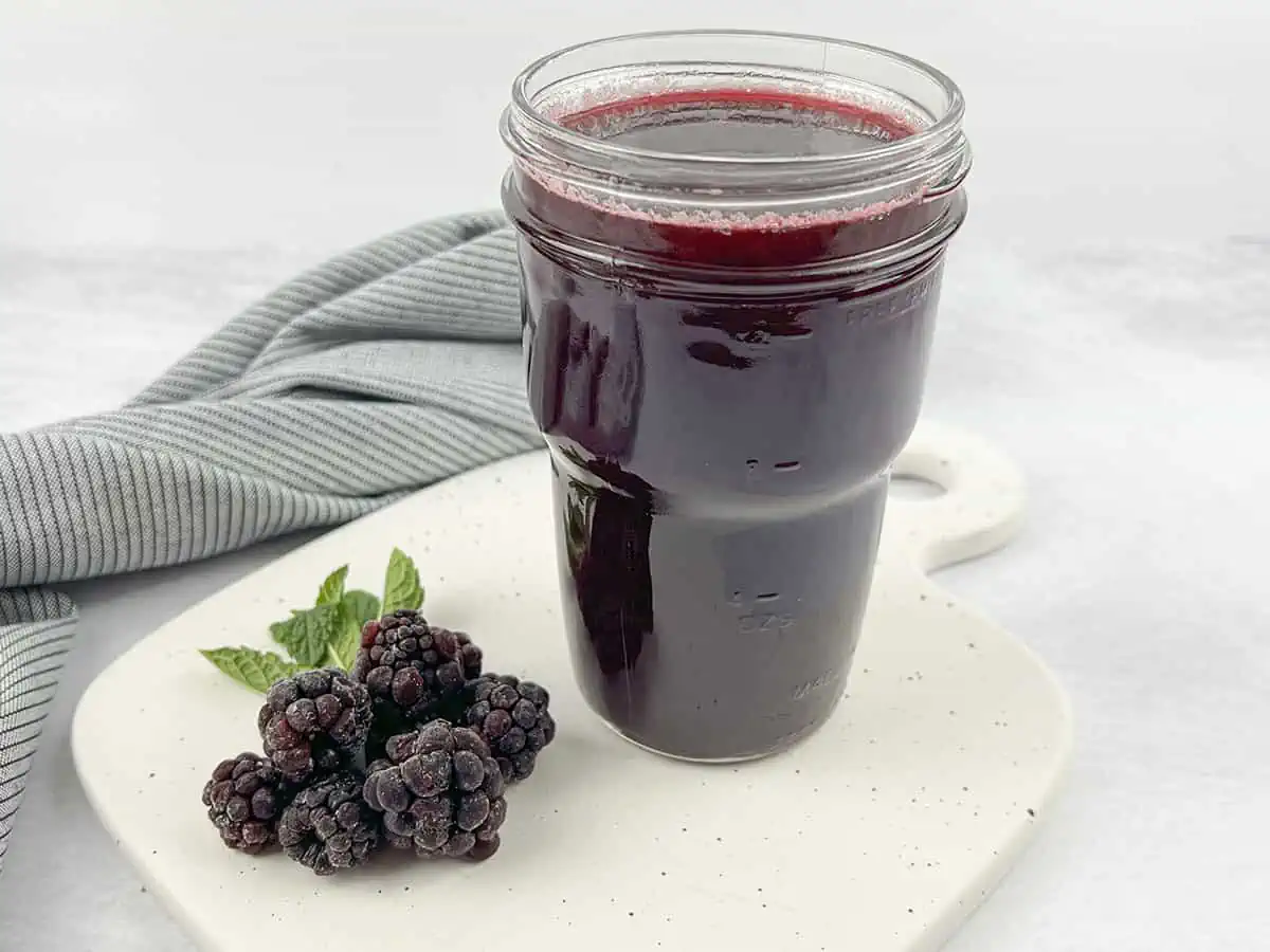 Blackberry syrup in a glass jar with berries on the left. 